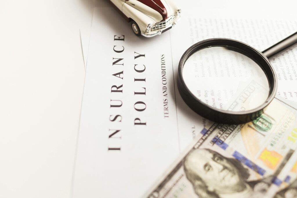 pexels-photo-10341357-10341357 Close-up image of an insurance policy with a magnifying glass, money, and toy car.