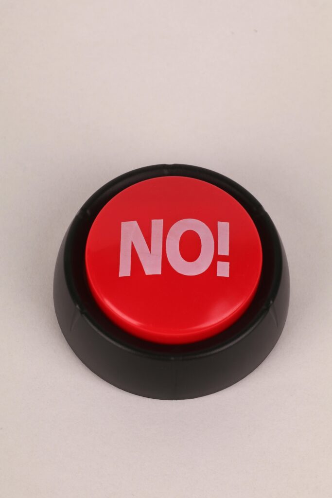A close-up of a red button with the word 'NO' on a beige background, emphasizing refusal or denial.