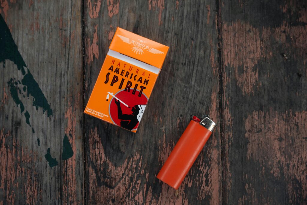 Orange Natural American Spirit cigarette pack with lighter on rustic wooden background.