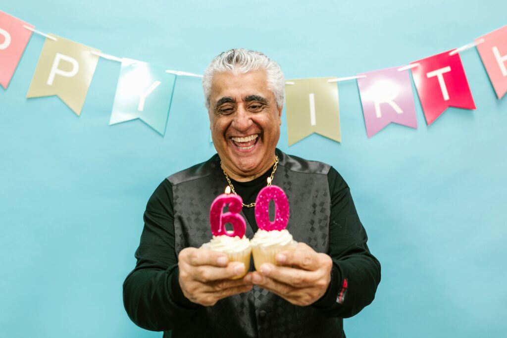 Smiling senior man holding cupcakes with 60 candles at a birthday party.